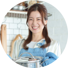 キッチンに立っている笑顔の女性が両手で鍋を持っている写真